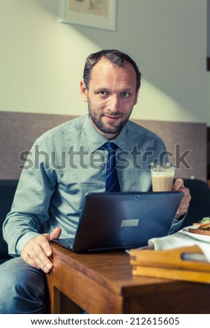 Businessman eating breakfast at home/hotel. Indoor photo. He is working on laptop pc.