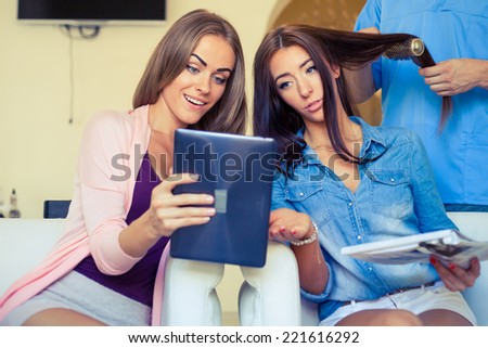 Beautiful woman showing hairstylist on a tablet examples hairstyle in hairdressing salon