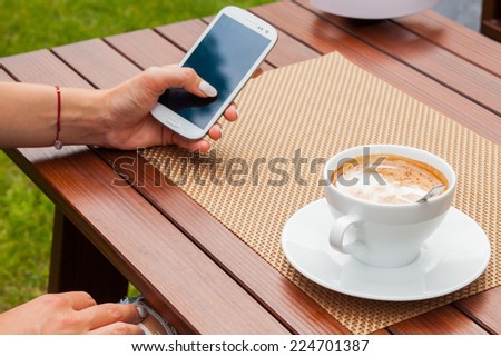 Women hands with mobile phone coffee on the table. Outdoor photo. Copy space
