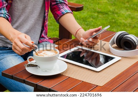 Women hands with tablet computer,mobile phone, headphones and coffee on the table. Outdoor photo. Copy space