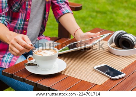 Women hands with tablet computer,mobile phone, headphones and coffee on the table. Outdoor photo. Copy space