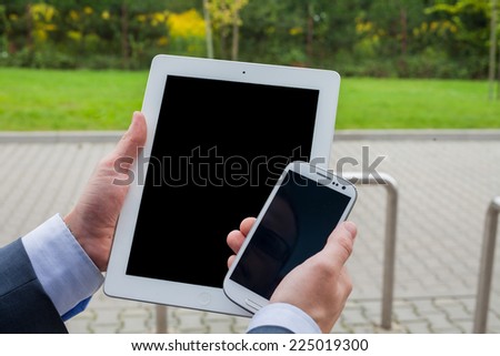 Close up of businessman hands with mobile phone and tablet pc on a park background. Copy space