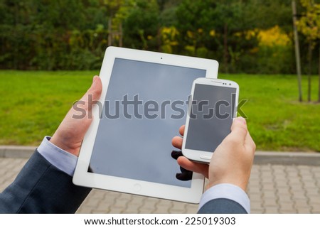 Close up of businessman hands with mobile phone and tablet pc on a park background. Copy space