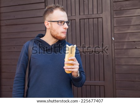 Hungry bearded customer eating delicious fast food: hotdog. Outside photo