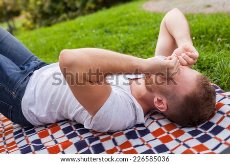 Sad young man lying in the summer park with Hidden Face. He is crying. Outdoor photo