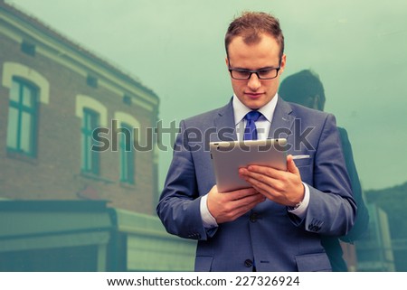 Caucasian businessman outside office using white tablet pc on a office block background. Copy space.