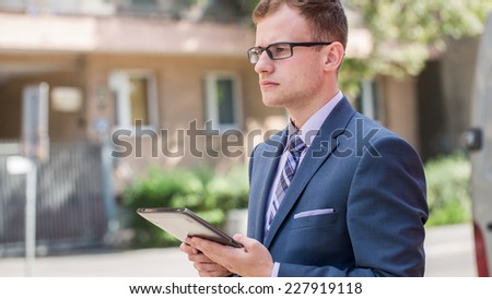 Caucasian businessman outside office using white tablet pc on a office block background. Copy space.