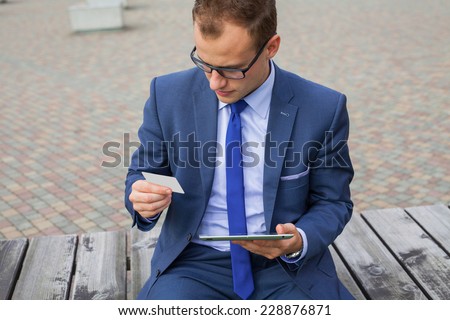Caucasian businessman outside office using white tablet pc on a office block background. Copy space