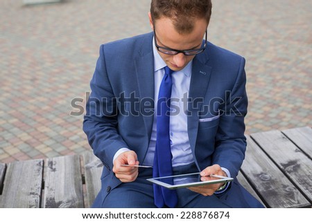 Caucasian businessman outside office using white tablet pc on a office block background. Copy space