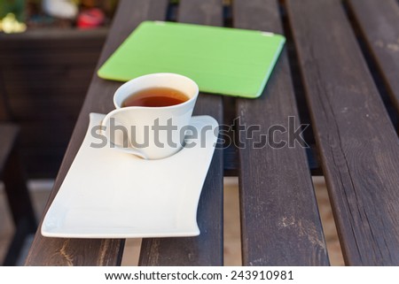 Tablet pc in green cover and cup of tea on wooden table. Relax concept. Outdoor photo.