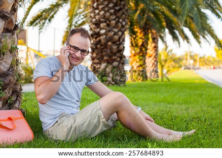Young tourist sitting under palm tree with mobile phone. Positive emotion. Vacation time.