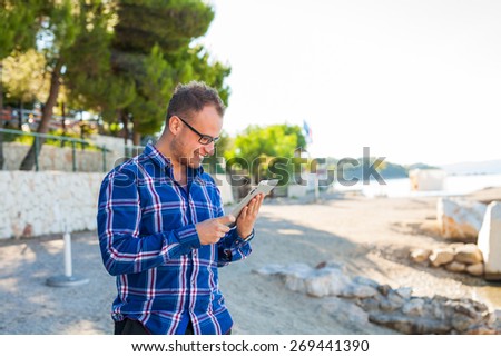 Young tourist in shirt with mobile tablet pc on a beach. Positive emotion. Vacation time.