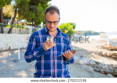 Young tourist in shirt with mobile phone and tablet pc on a Croatian beach. Positive emotion. Vacation time.