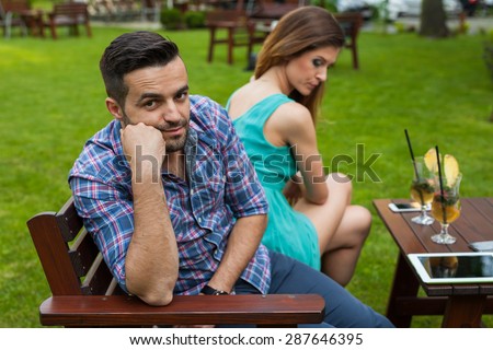 Couple sitting on the bench in the garden. They are taking offense and sitting back to back