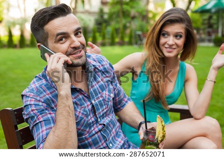 Couple sitting on the bench in the garden restaurant. Man is talking by the phone