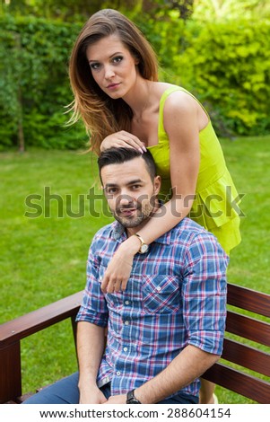 Man sitting on  bench in the garden. Girl standing behind him. Positive emotions