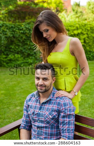 Man sitting on  bench in the garden. Girl standing behind him. Positive emotions