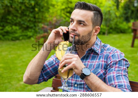 Man sitting on the bench in the garden, talking by the phone and drinking.