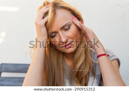 Blond hair girl sitting behind the table and suffering because of her head