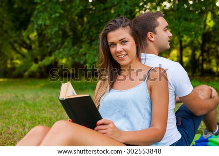 Couple having picnic. Pretty girl reads. Man is using tablet.