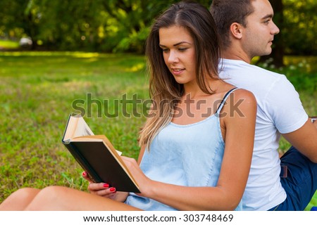 Couple having picnic. Pretty girl reads. Man is using tablet.