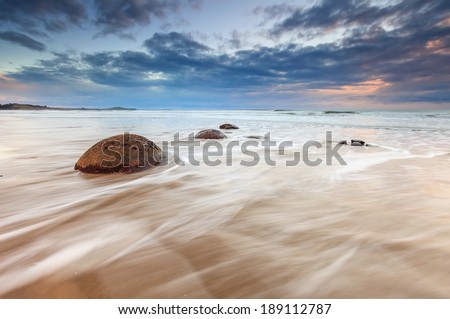 Moeraki Boulders beach, during cloudy sunrise with waves flowing over, South Island, New Zealand