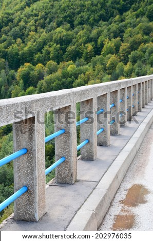 The series of concrete columns, reinforced with blue pipes, as a bridge guard rail. Landscape with forest and concrete bridge