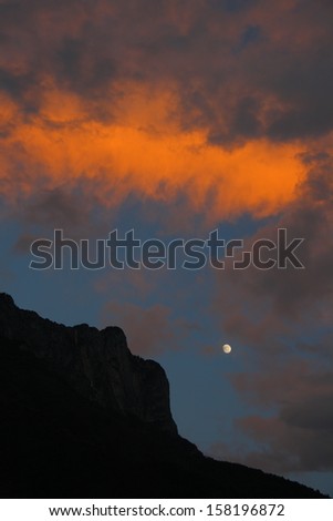 Silhouette of the summit of beautiful Gemu holy mountain and moon in flaming evening glow, Yunnan, China