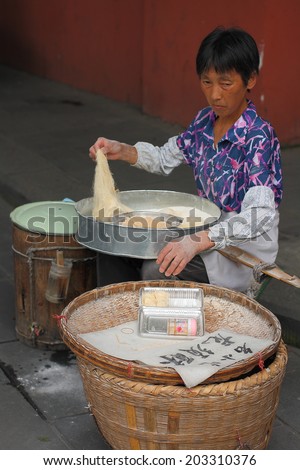 CHENGDU, CHINA - JULY 5: Unidentified woman makes and sells Asparagus Crisp, so called longxusu, a special Chinese dessert, near Wenshu monastery on July 5, 2014, Chengdu, Sichuan, China.