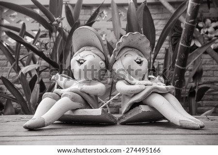 A girl and a boy dolls statue sitting swing seat in green park made black and white color.