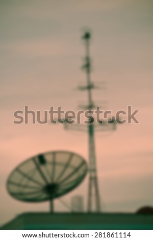 Blurred TV satellite dishes and antennas on roof at sunset.