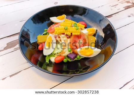 Salad of egg,corn, tomatoes, cucumbers, olives on a plate.