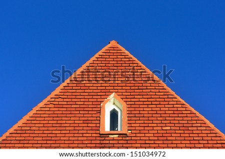 window in a roof attic with bricks against blue sky with triangle shape