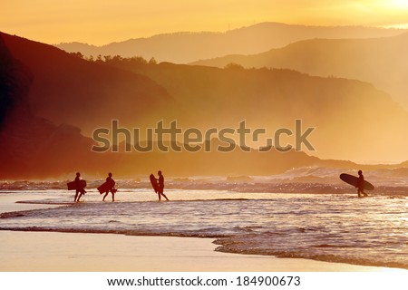 surfers and boogie boards on beach at sunset