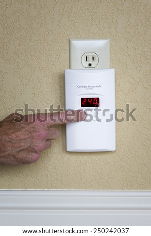 Closeup of a male hand pressing a button on a digital carbon monoxide alarm
