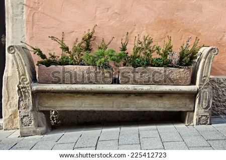 Vintage stone bench with flower beds stands against a wall in old town