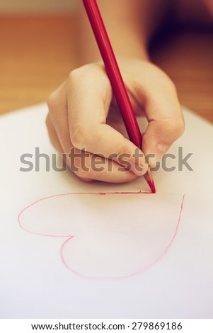 Child is drawing red heart by pencil, concept of love