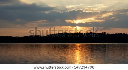 cloudy sky and the orange rays of evening sun on the beautiful waters of the silent lake