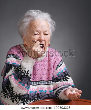 Old sick woman with pills on a gray background