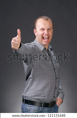 Super excited young man giving thumbs up on gray background