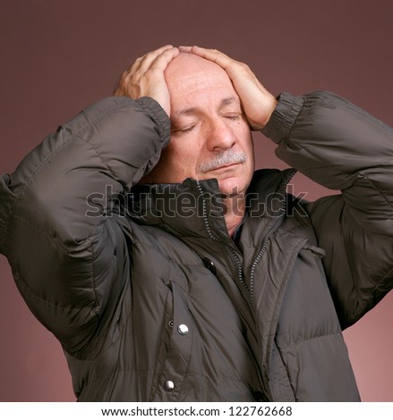 Portrait of a senior man suffering from bad headache on a brown background