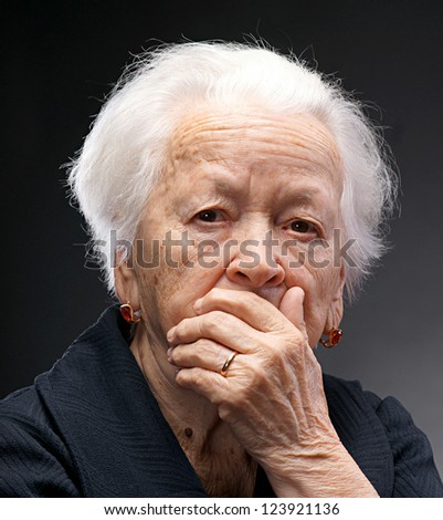 Old sad woman with hand on her face on a gray background