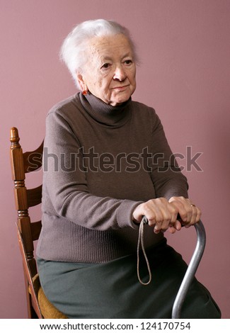 Old woman sitting on a chair with a cane on brown background