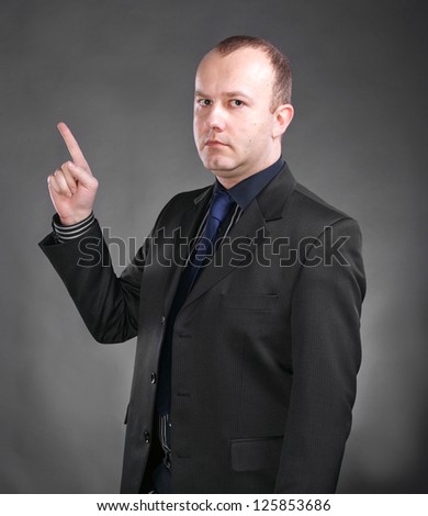 Portrait of seriousy young man pointing upwards on a gray background