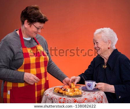 Mother and daughter having tea with apple pie on an orange  background