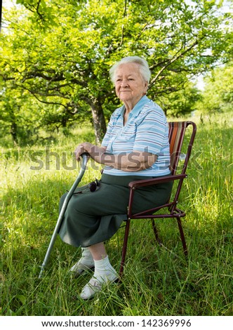Old woman sitting on a chair on nature background