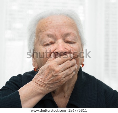 Old woman yawning with hand in front of her mouth
