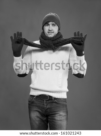 Handsome man in winter mittens, scarf and hat on a gray background