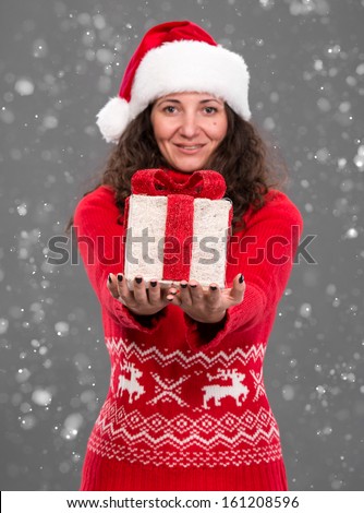 Smiling woman in santa hat with gift box, christmas, x-mas, winter, snow falls. Focus on box.
