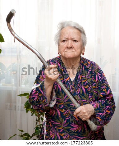 Old angry woman threatening with a cane at home